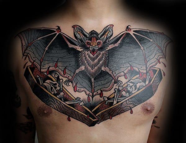 Large chest tattoo of a fierce bat with outstretched wings above two skeletons in coffins, detailed with blood drops and bold shading.