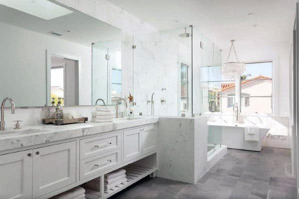 Modern bathroom with a grey marble countertop, dual sinks, glass shower, and large bathtub by a window