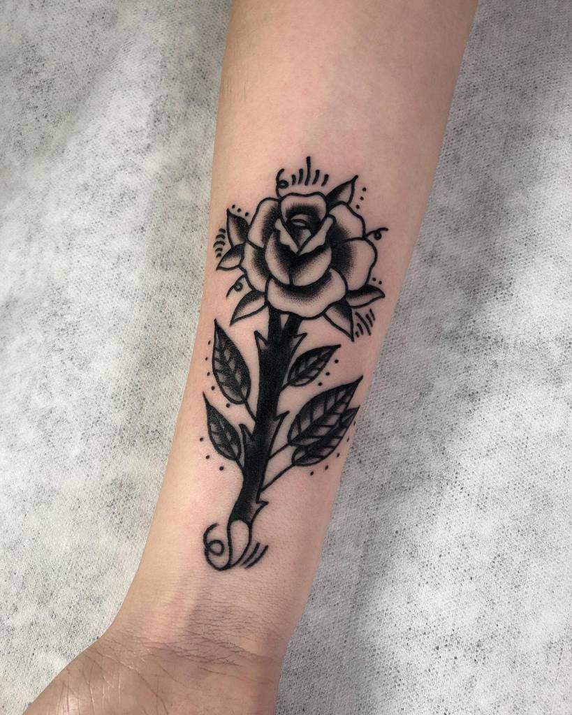 A tattoo of a black rose graces the forearm, its intricate details capturing shadows and light, creating an elegant symbol of beauty and mystery