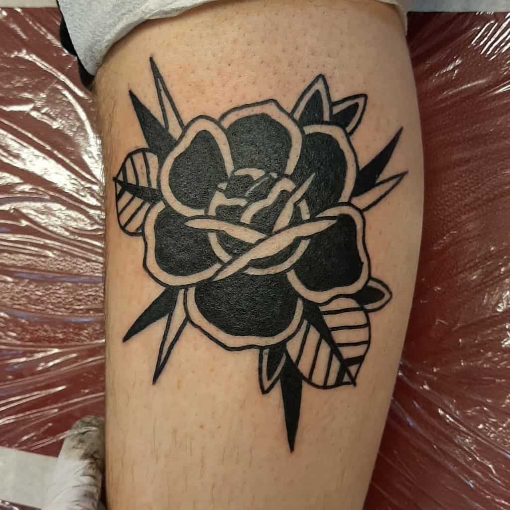Tattoo of a black and white rose with leaves on the back of a leg