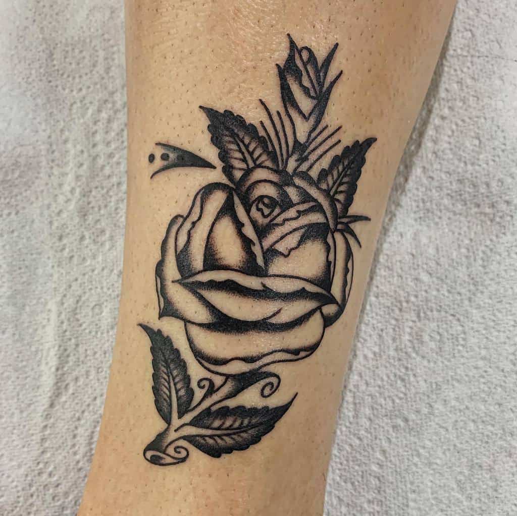 A striking black and gray rose tattoo with intricately detailed leaves elegantly graces the forearm