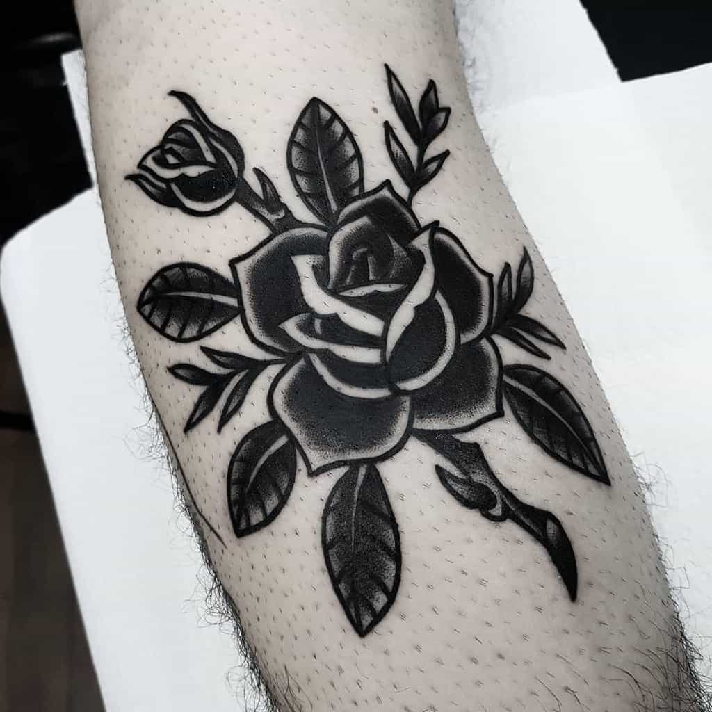 Black and white rose tattoo with leaves on a forearm