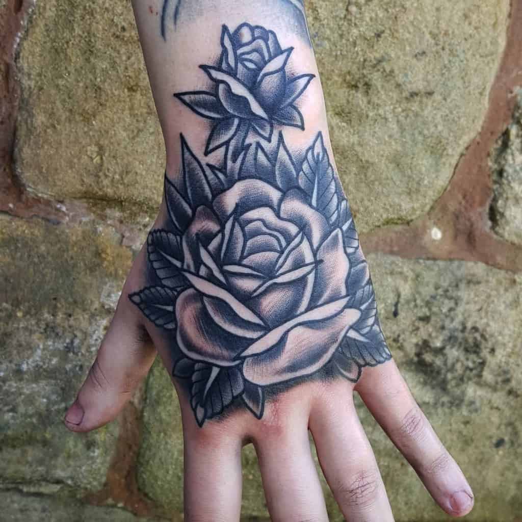 A hand adorned with intricate black and whitw rose tattoos