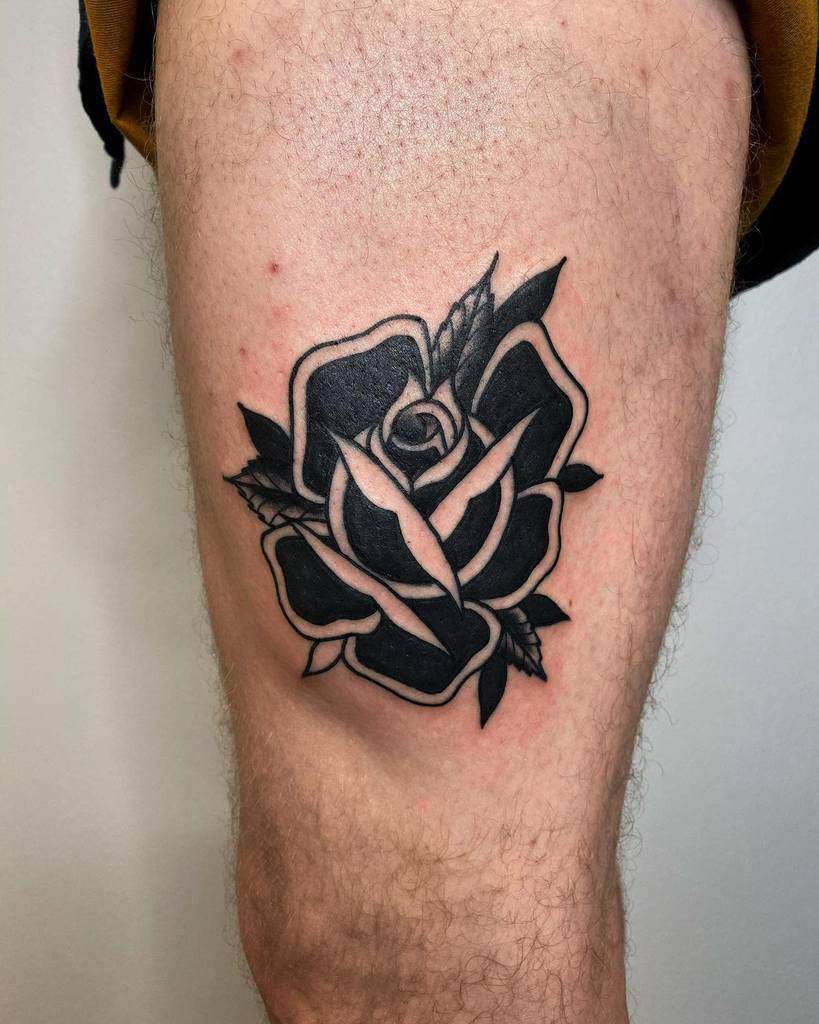 Black and white rose tattoo on a person's leg, featuring bold outlines and leaf detail