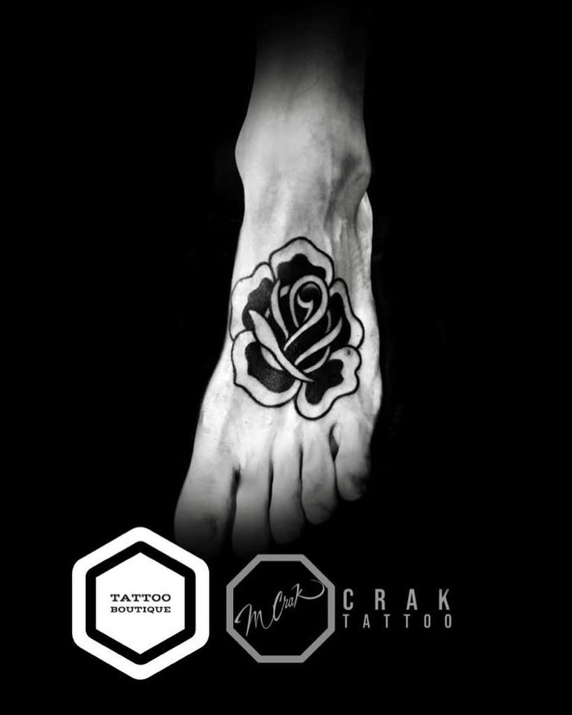 A black and white rose tattoo on the top of a foot