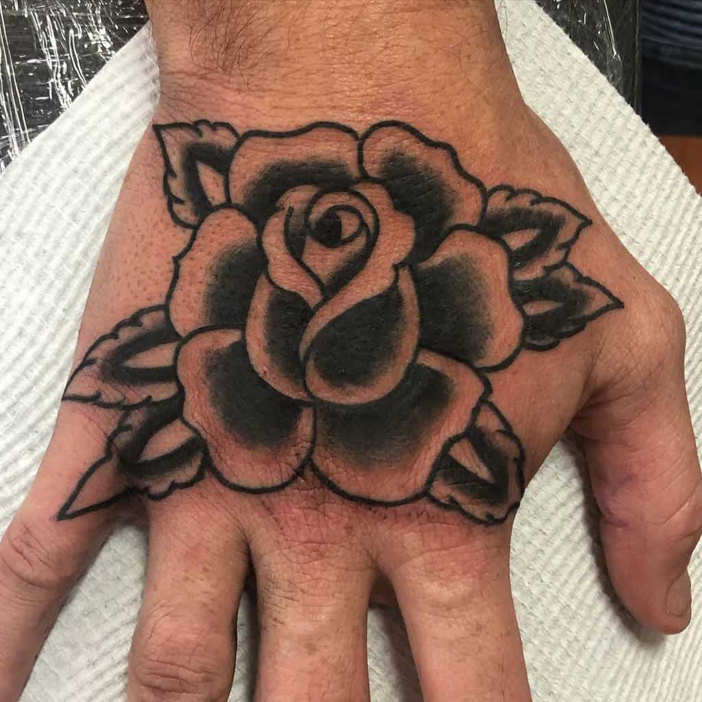 Tattoo of a dark rose with leaves on the back of a hand
