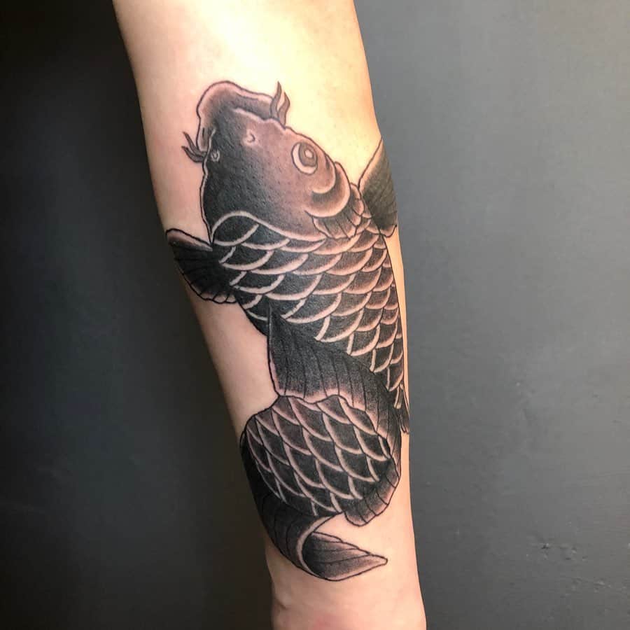 Black koi fish tattoo on forearm, depicted swimming upwards with detailed scales