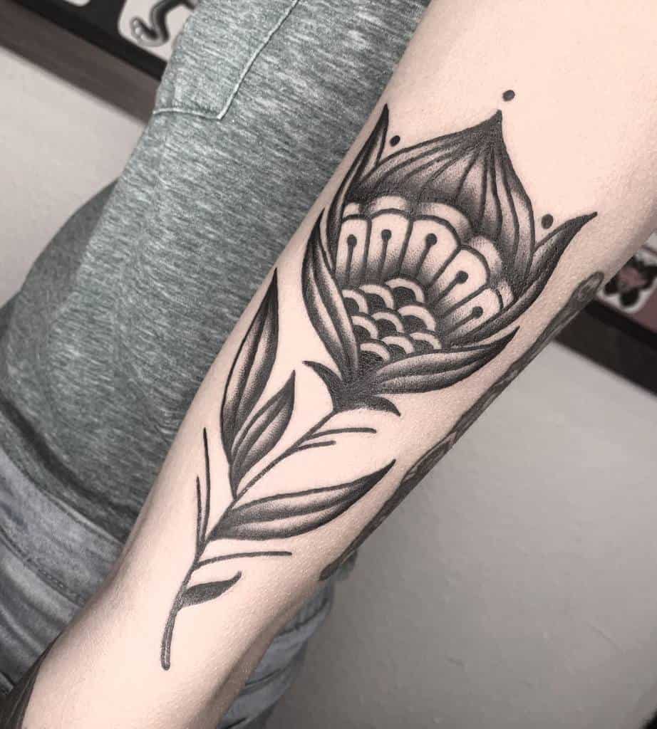 Tattoo of a stylized, symmetrical flower in black ink on arm, featuring bold lines and pointed petals