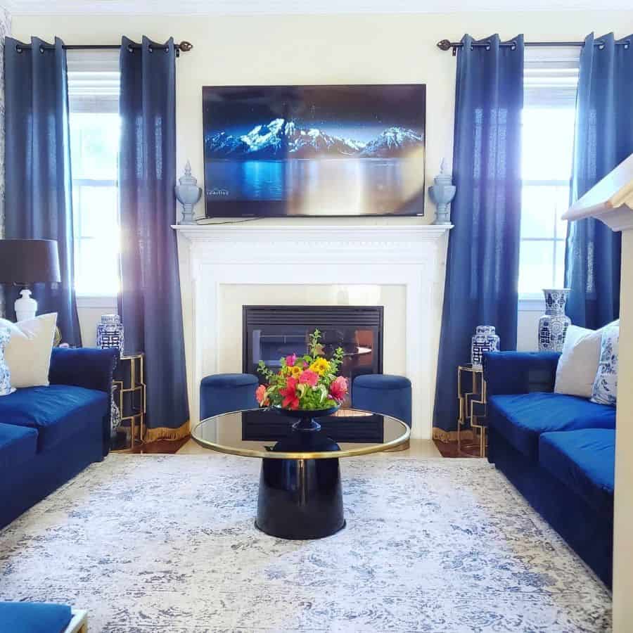 Traditional living room with navy blue sofas, matching curtains, a white fireplace, and a modern round coffee table centerpiece.