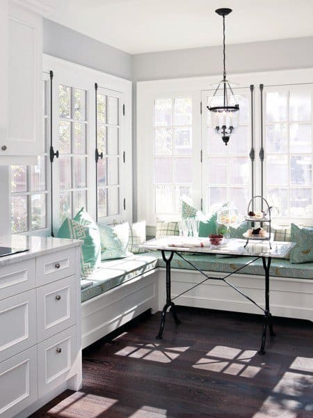 Bright kitchen nook with white cabinets, cozy corner seating, decorative pillows, and a stylish black pendant light
