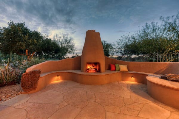 Outdoor seating area with a central fireplace, surrounded by trees and a cloudy sky background