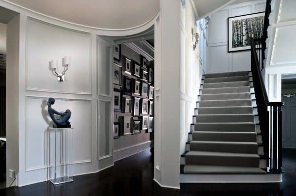 Art-filled stylish hallway with a white staircase, dark wooden floor, and sculpture displayed in the corner