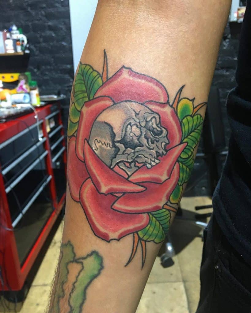 A vibrant tattoo of a skull nestled within a vivid red rose graces the forearm