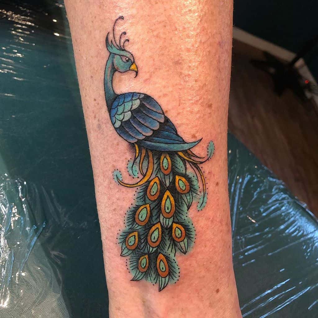Peacock tattoo with vibrant blue and green feathers, adorned with orange details, on the forearm.