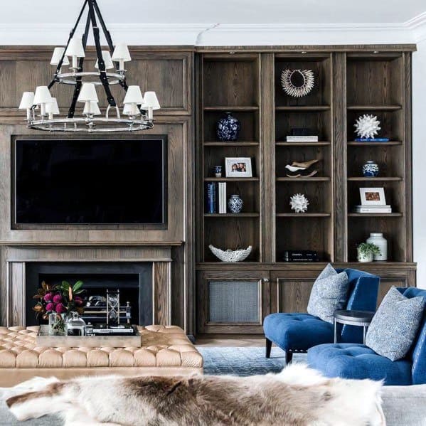 Cozy living room with wood paneling, TV, fireplace, blue chairs, and a decorative bookshelf