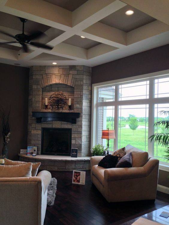 Stone corner fireplace with dark wood mantel in a cozy living room featuring large windows.