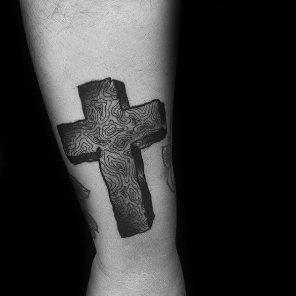 Black ink cross tattoo with topographic map-style line detailing, giving it a textured, dimensional look on the calf.