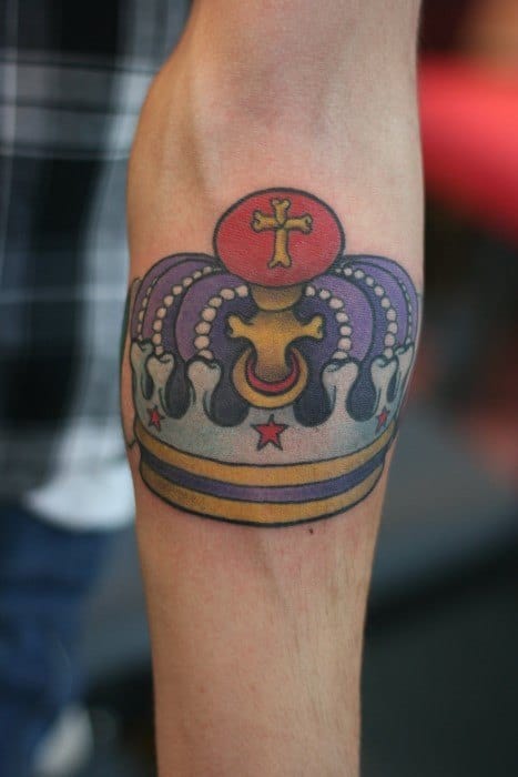 Colorful traditional crown tattoo on the forearm with red stars, gold accents, and purple detailing for a bold royal look.