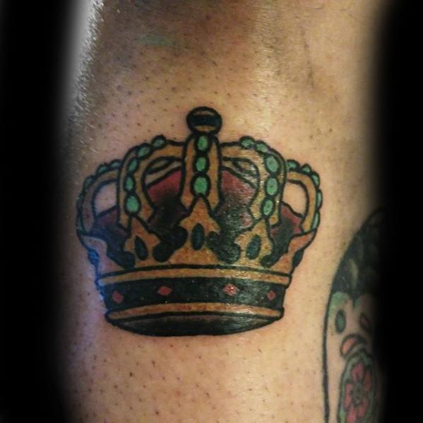 Traditional crown tattoo with gold, green, and red accents, featuring bold black outlines and jewel-like detailing.
