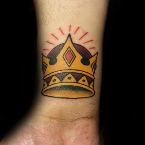 Bold traditional crown tattoo on the wrist with gold, red, and blue details, highlighted by red rays for a radiant effect.