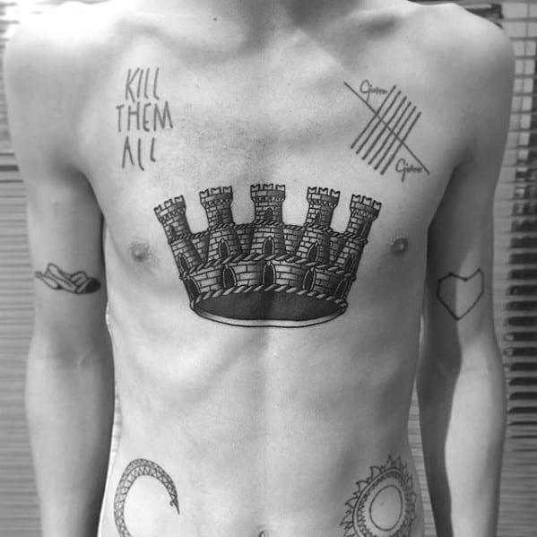 Black and grey chest tattoo of a castle-shaped crown with stone detailing, centered below the chest for a medieval-inspired look.