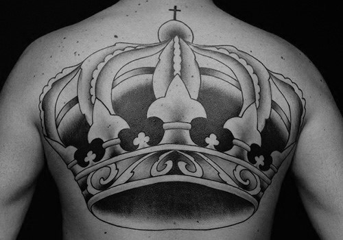 Large black and grey tattoo of a royal crown across the upper back, featuring bold shading and intricate ornamental details.