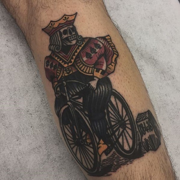 Traditional tattoo of a skeleton king of clubs riding a bicycle, blending dark humor and vintage playing card style.
