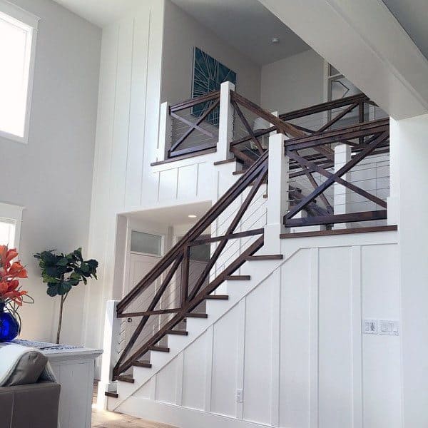 Modern staircase with wooden railings, white panel walls, a tall plant, and a decorative art piece