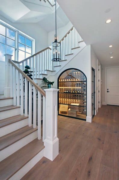 A modern staircase with wooden steps, white railings, a large window, and an illuminated wine cellar beneath