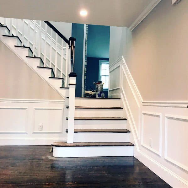 A staircase with white railings and dark wooden steps in a brightly lit room with chair rail wainscoting
