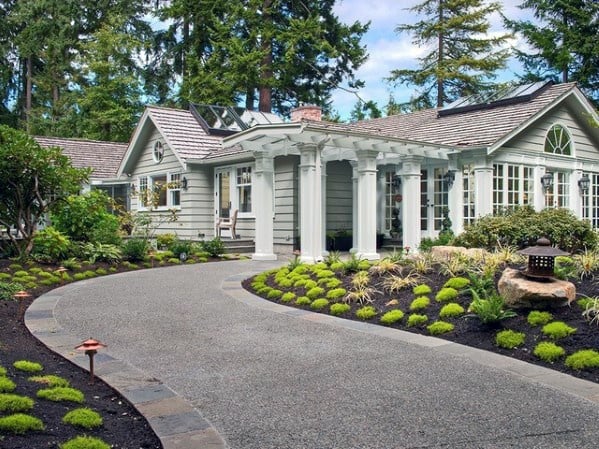 Curved asphalt driveway bordered with stone edging, surrounded by well-manicured landscaping.