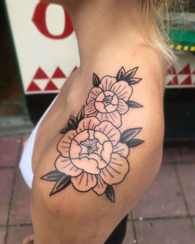 A delicate tattoo of two outlined flowers graces the shoulder, their leaves elegantly extending. The petals are lightly shaded, adding a touch of softness