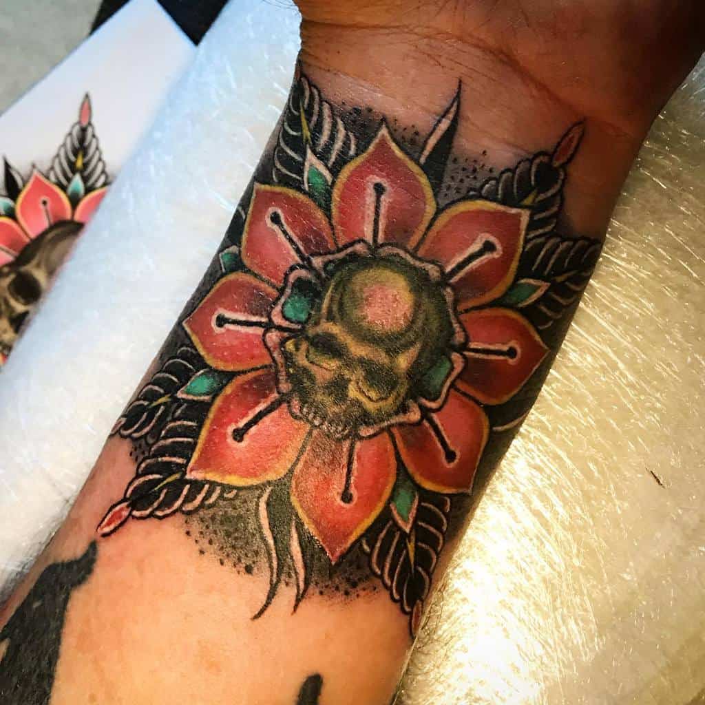 Traditional style flower tattoo with bold colors, featuring a skull in the center, placed on the wrist