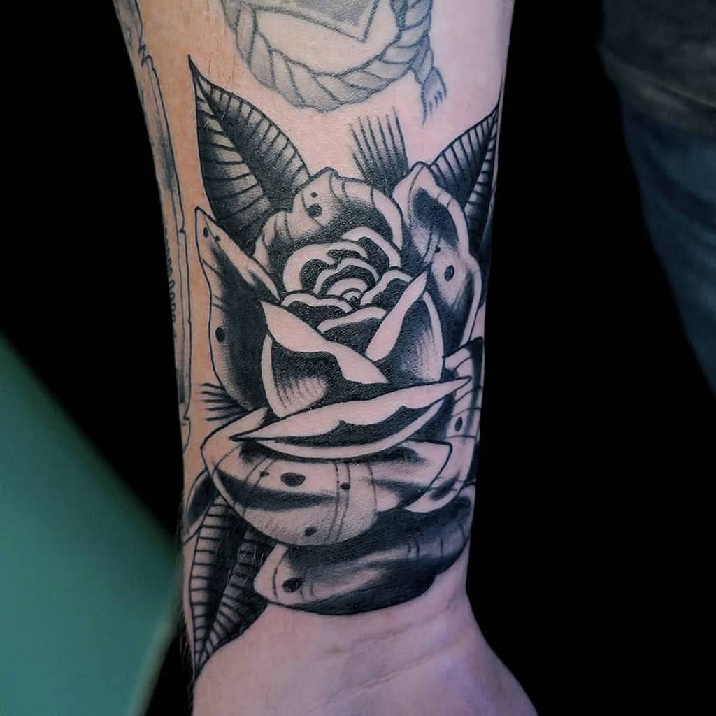 A black and gray tattoo of a rose with leaves gracefully extends from the wrist up the arm