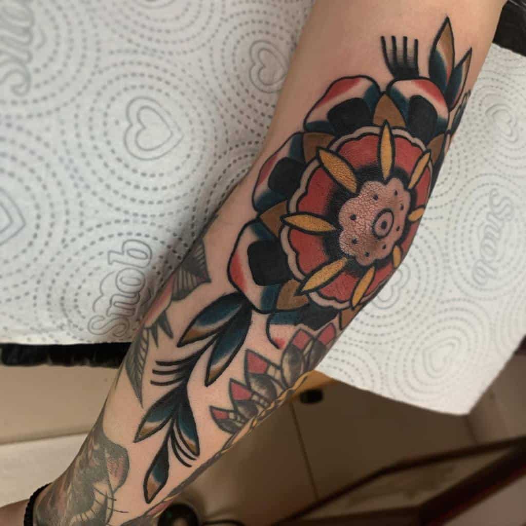 A forearm with a colorful floral tattoo in traditional style, featuring bold outlines and vivid colors