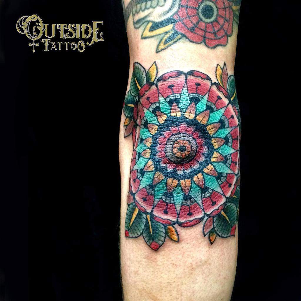 Colorful mandala tattoo featuring geometric patterns and leaves on an arm