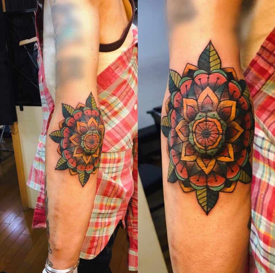 Colorful mandala flower tattoo on a person's upper arm, with red and green hues and detailed shading