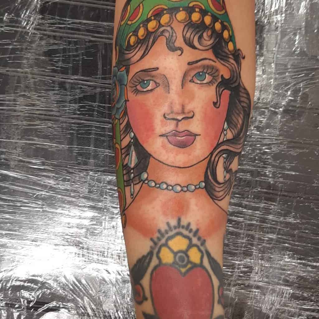 A mesmerizing tattoo of a gypsy woman's face adorns the arm, vibrant colors bringing its details to life with an enchanting allure