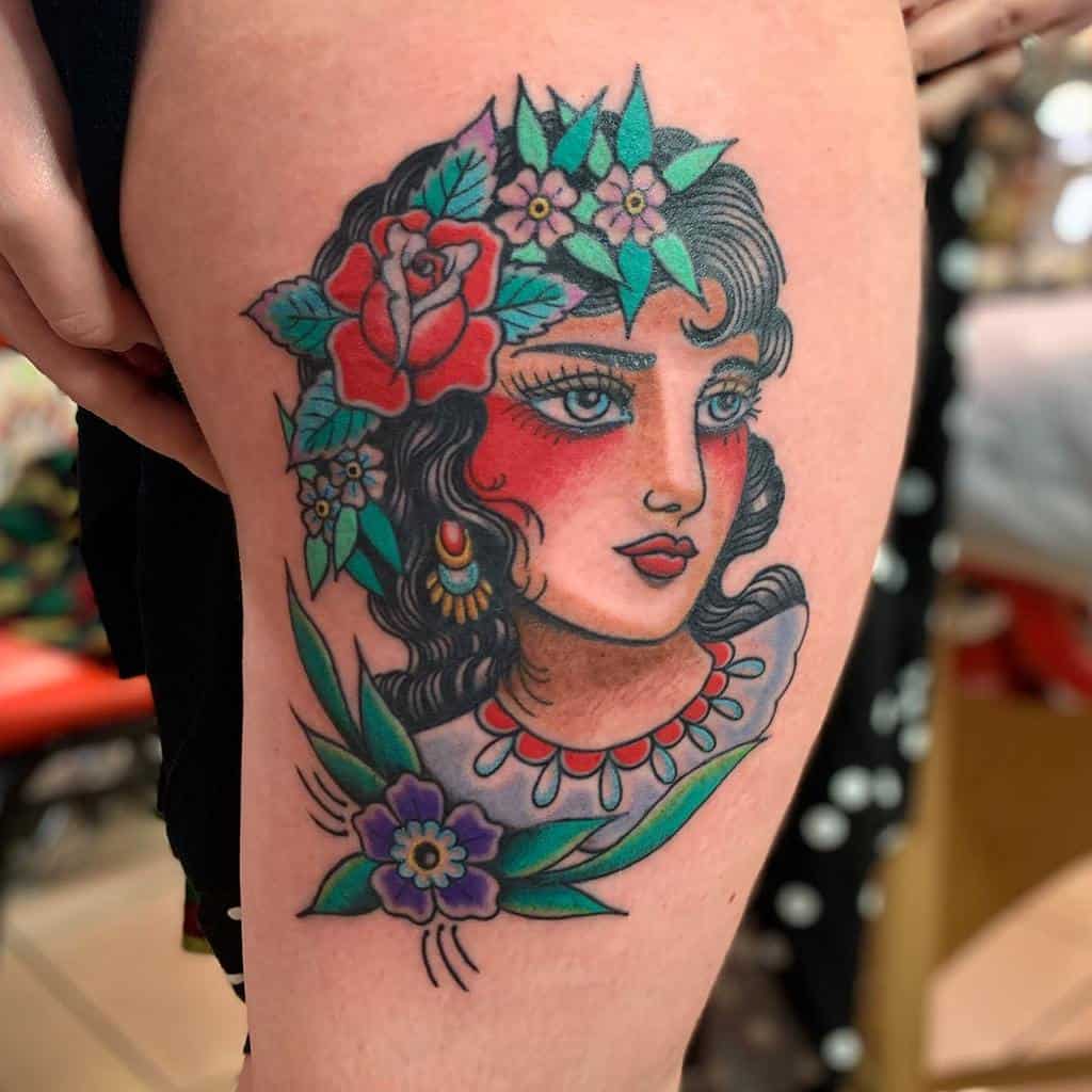 Colorful tattoo of a gypsy woman's face adorned with vibrant floral decorations on an arm