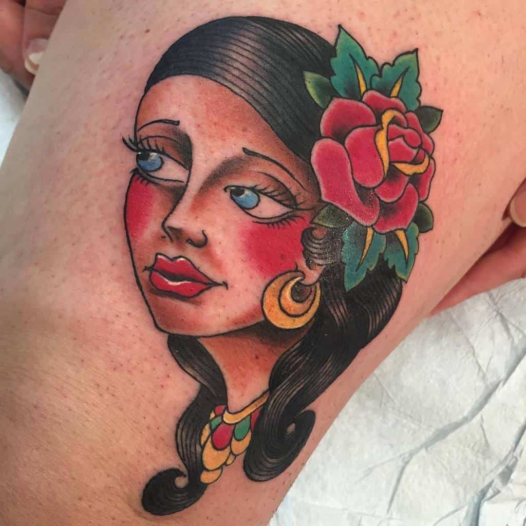 Tattoo of a gypsy woman's face adorned with a flower in her hair and colorful accessories