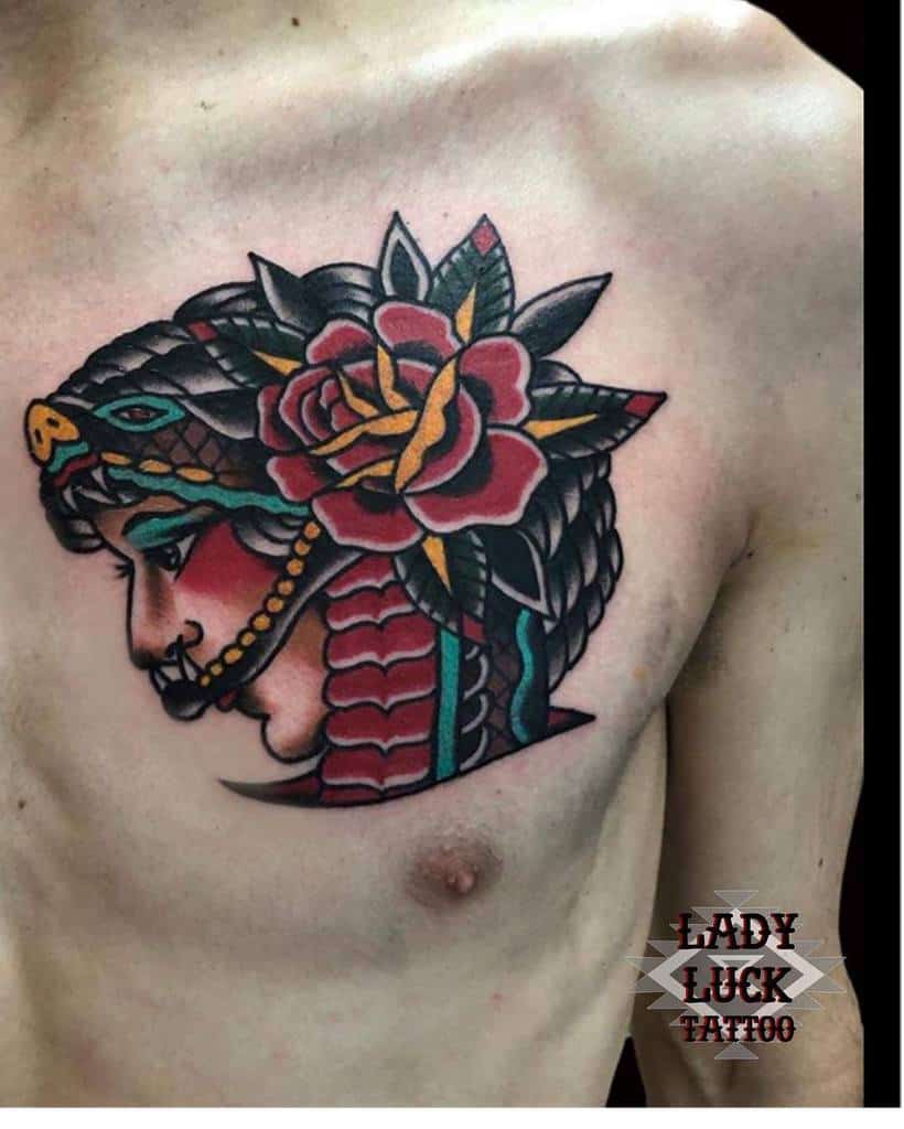 Tattoo of a gypsy woman's face adorned with a snake headdress, accented by a large rose on man's chest