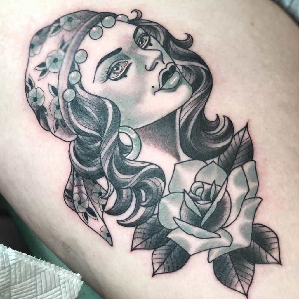 Tattoo of a gypsy woman's face adorned with a floral headscarf and a rose beneath her, gracefully etched on the skin