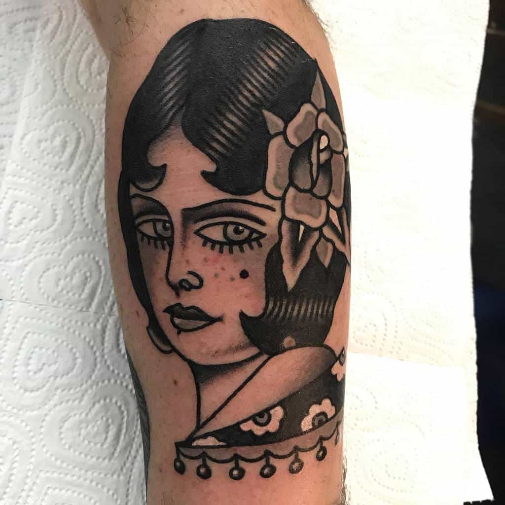 Tattoo of a gypsy woman's face with a vibrant flower in her hair, elegantly inked on a leg
