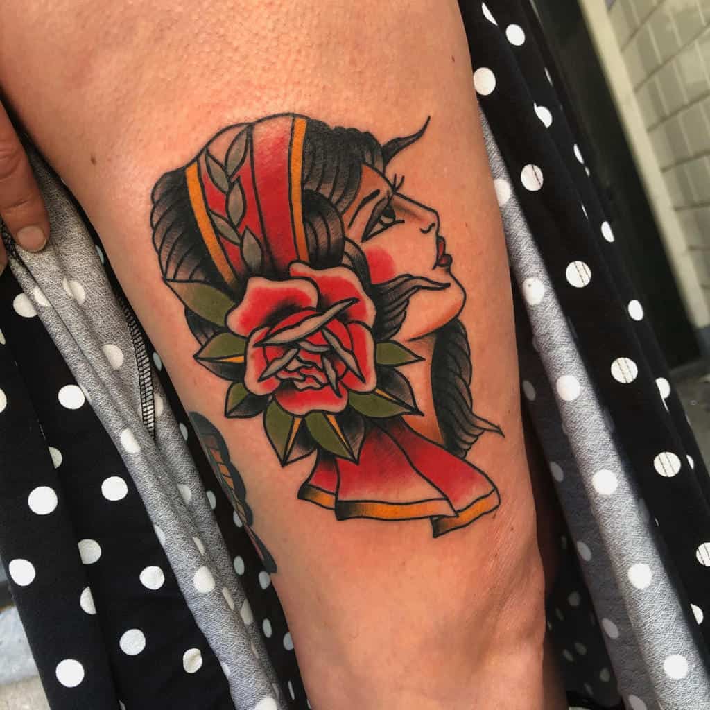 Vintage-style tattoo of a gypsy woman's profile adorned with dark hair and a striking red rose