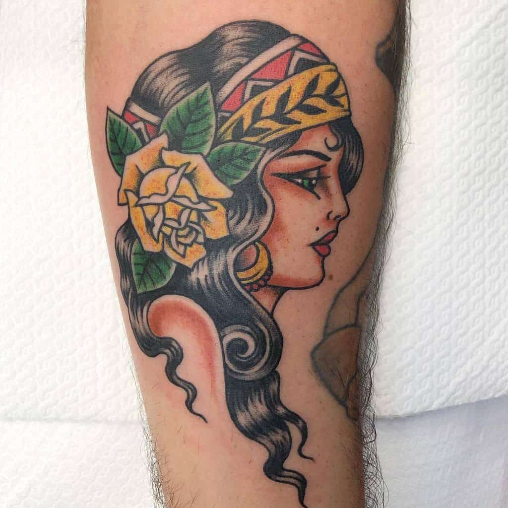 Tattoo of a gypsy woman's profile adorned with a yellow rose and headband, rendered in traditional style