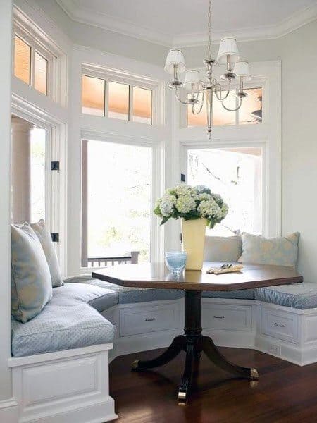 Cozy nook with bench seating, round table, floral centerpiece, and chandelier lighting basked in natural light