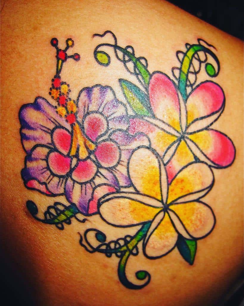 Colorful tattoo featuring a purple and red hibiscus flower alongside a yellow and pink plumeria, with swirling vine details on a shoulder