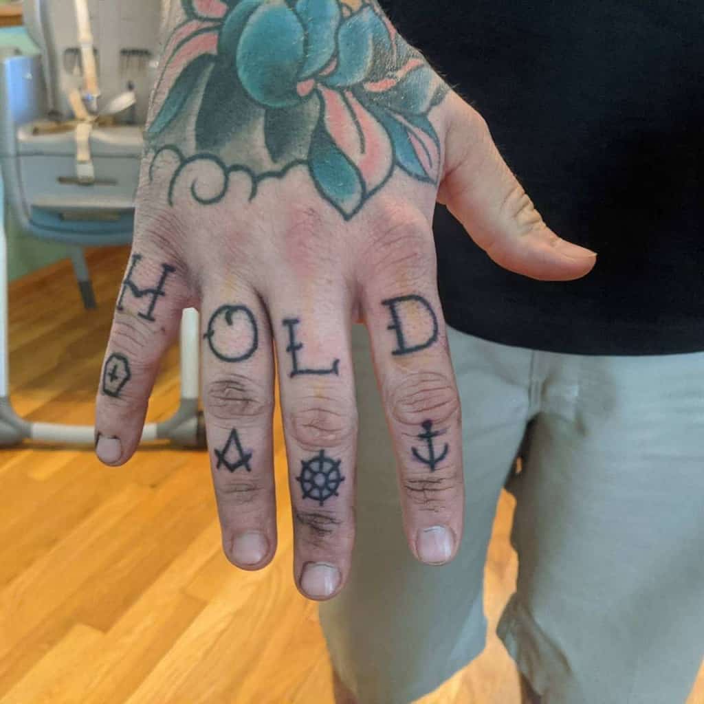 Hand with letters "HOLD" and symbols tattooed on fingers, floral tattoo on top of hand