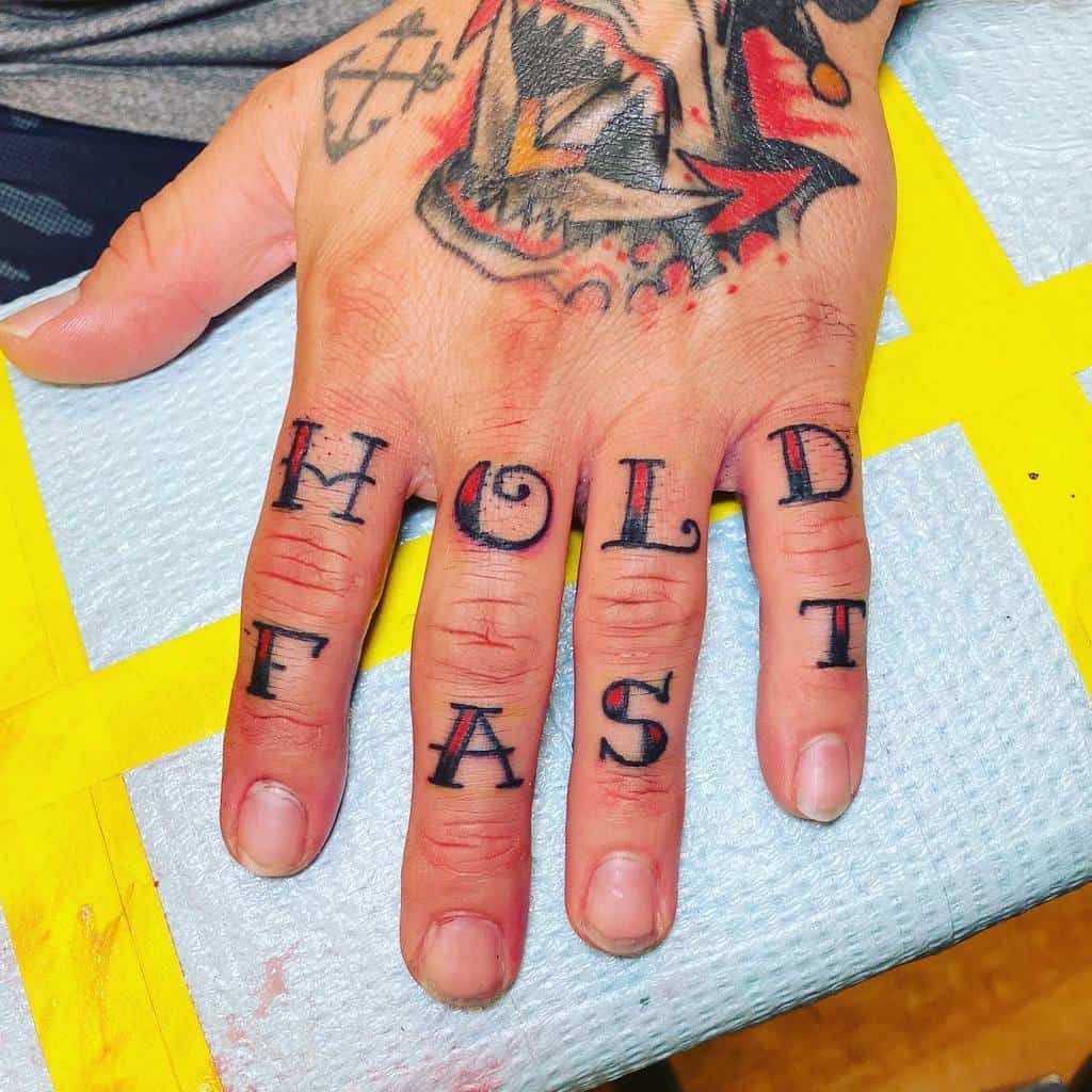 Close-up of hand with "HOLD FAST" tattooed on fingers