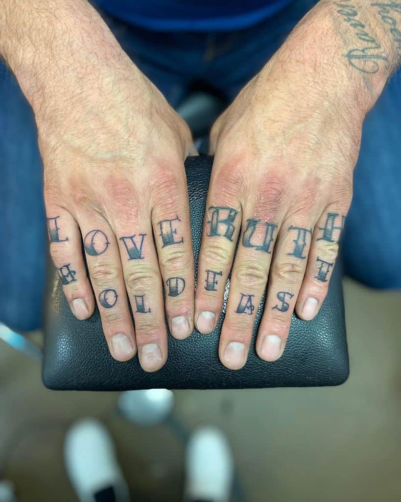 Hands with tattoos spelling "LOVE," "RUTH," and "HOLD FAST" on fingers